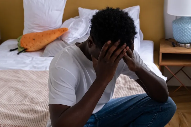 man sitting on bed with head in hands