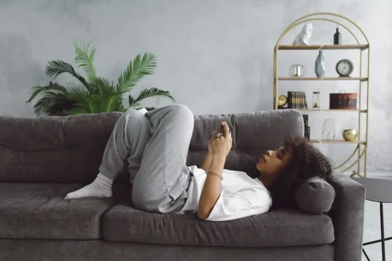 young woman laying on sofa using phone