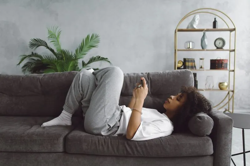 young woman laying on sofa using phone