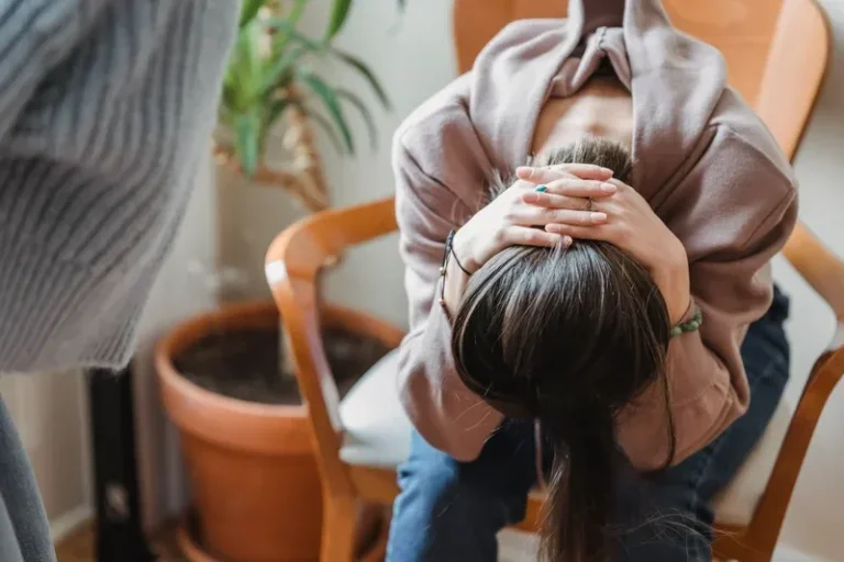 woman sitting bent over with hands clasped over head