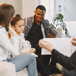 parents and child sitting on sofa smiling while talking to woman opposite