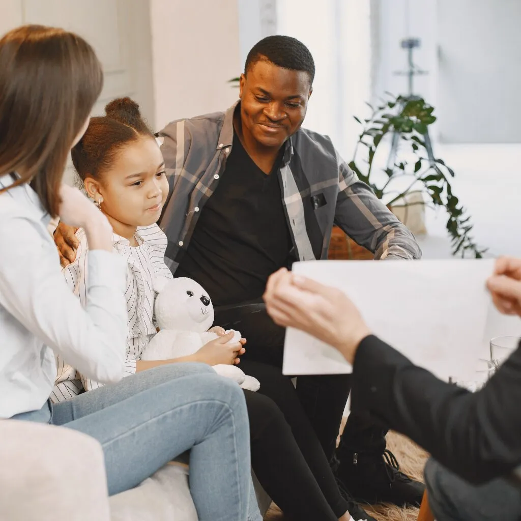 parents and child sitting on sofa smiling while talking to woman opposite